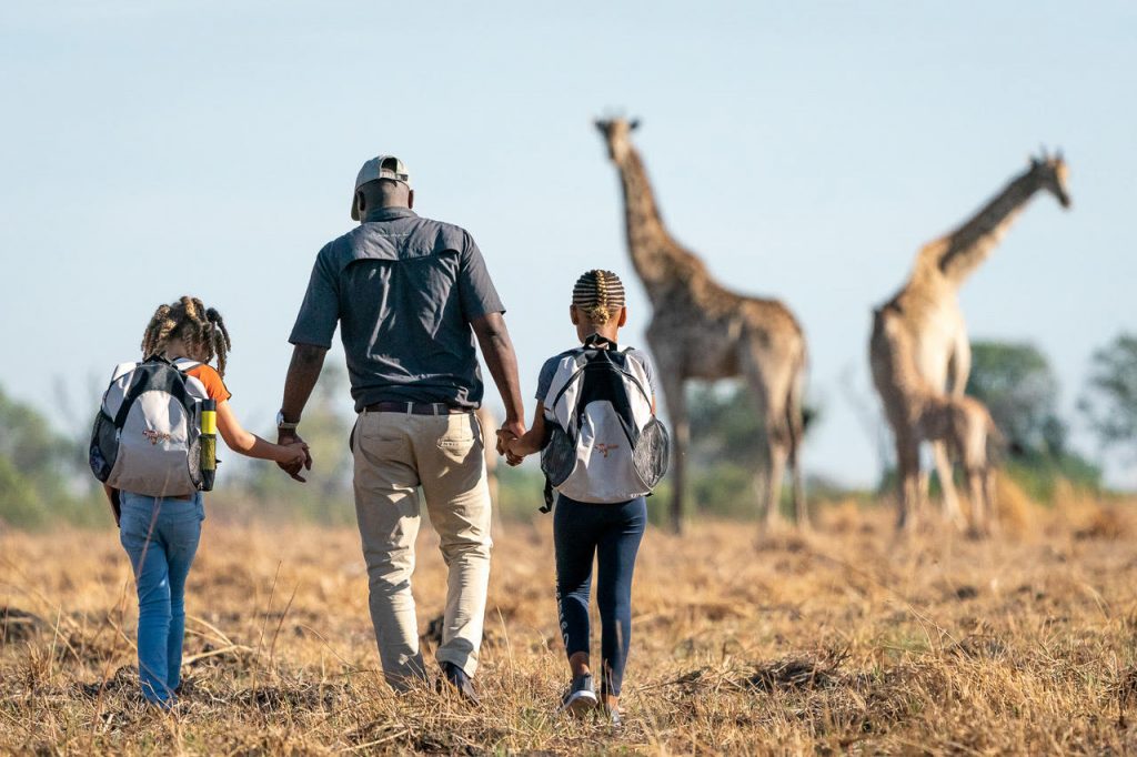Guide walking with kids while giraffe are watching in the background on African Safari holiday